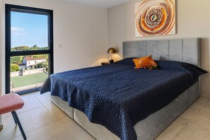 A bedroom with a bed, a nightstand, a lamp, a window, and a painting.