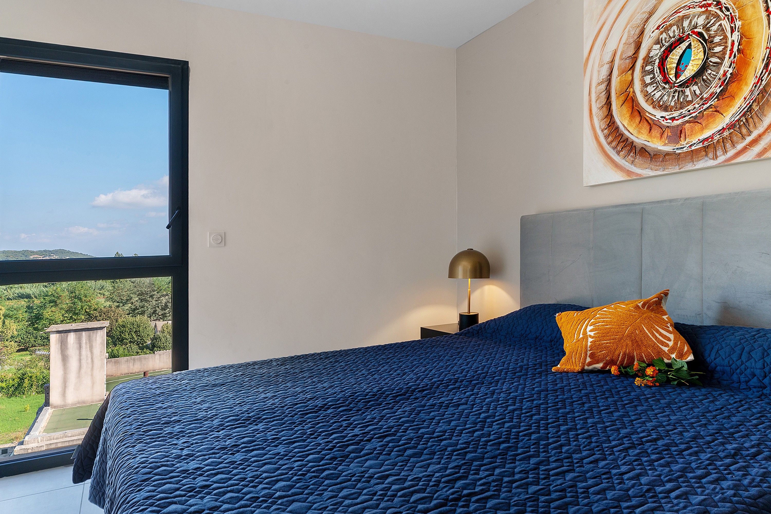 Ein Schlafzimmer mit einem großen Bett, einem Nachttisch, einer Lampe und einem Wandbild.