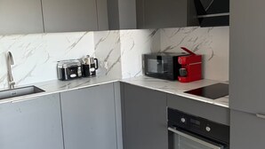 A modern kitchen with grey cabinets, a marble backsplash, a built-in microwave, a red coffee machine, and a stainless steel oven.