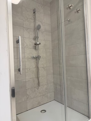 Une douche fermée par des parois en verre, dotée d’un pommeau de douche à main, d’un robinet mural et d’un panneau de commande.