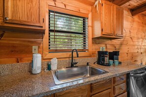 A kitchen with wooden cabinetry, a granite countertop, a stainless steel sink, and a window with blinds. - Starlit Ridge - Hot tub Fire Pit Mountain Views (Sevierville)