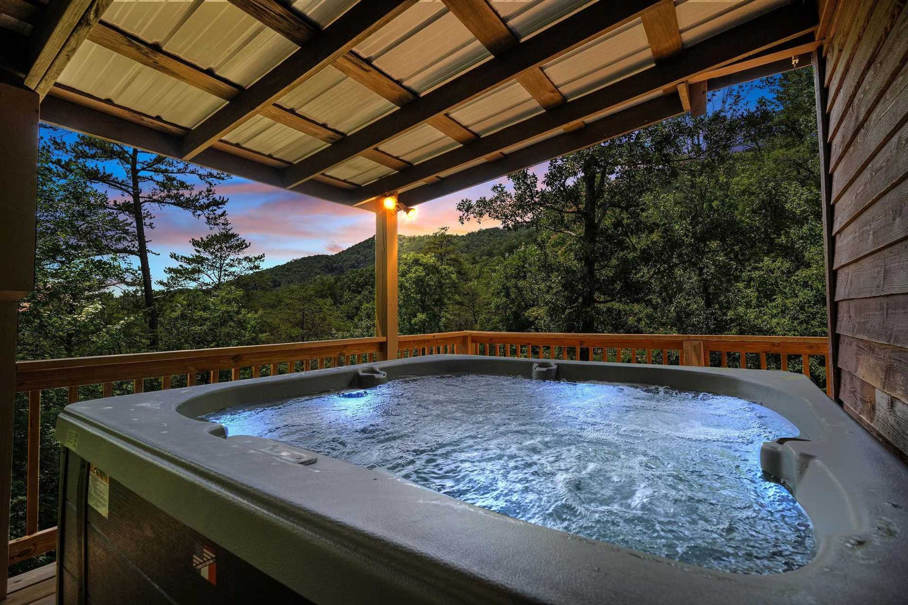 A hot tub with a wooden deck and a view of a forested hillside.