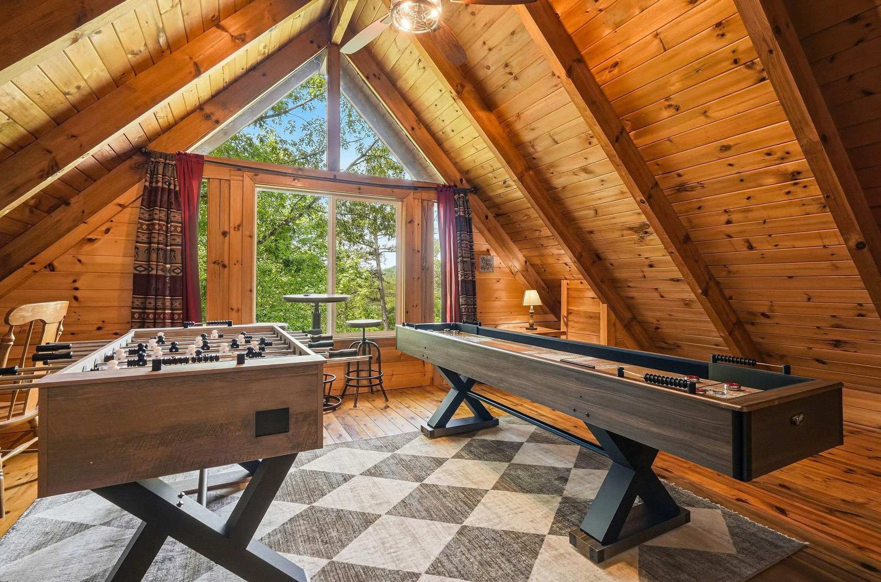 A cozy attic room with a foosball table, a pool table, and a large window offering a view of the outdoors.