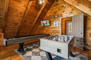 Ein Zimmer mit Tischfußball, Billardtisch und einem an der Wand befestigten Fernseher.