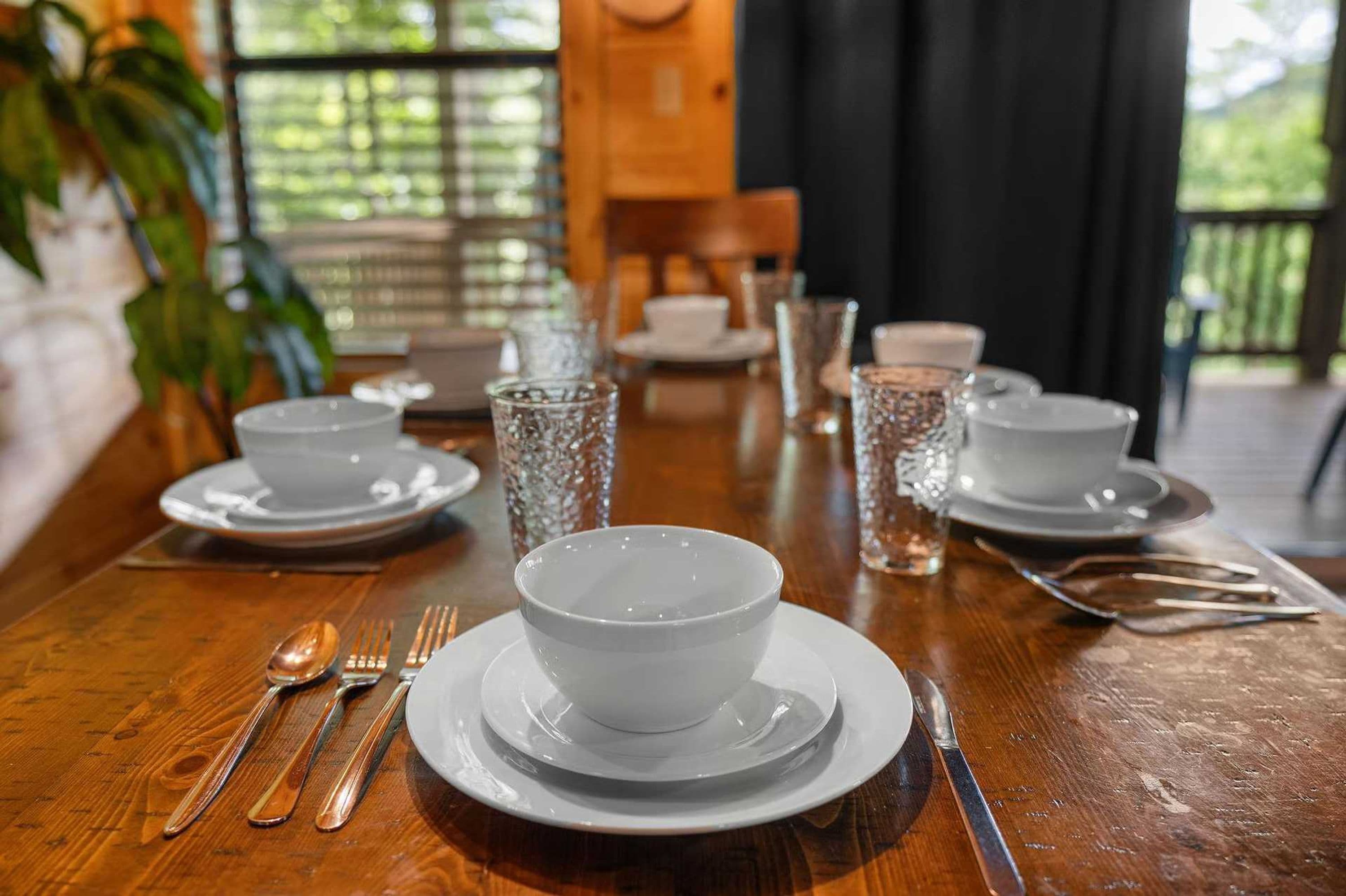 Une table à manger dressée avec des assiettes, des bols, des couverts et des verres, le tout de couleur blanche.