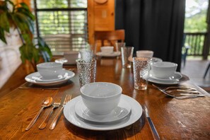 Una mesa de comedor dispuesta con platos, tazones, cubiertos y vasos blancos.