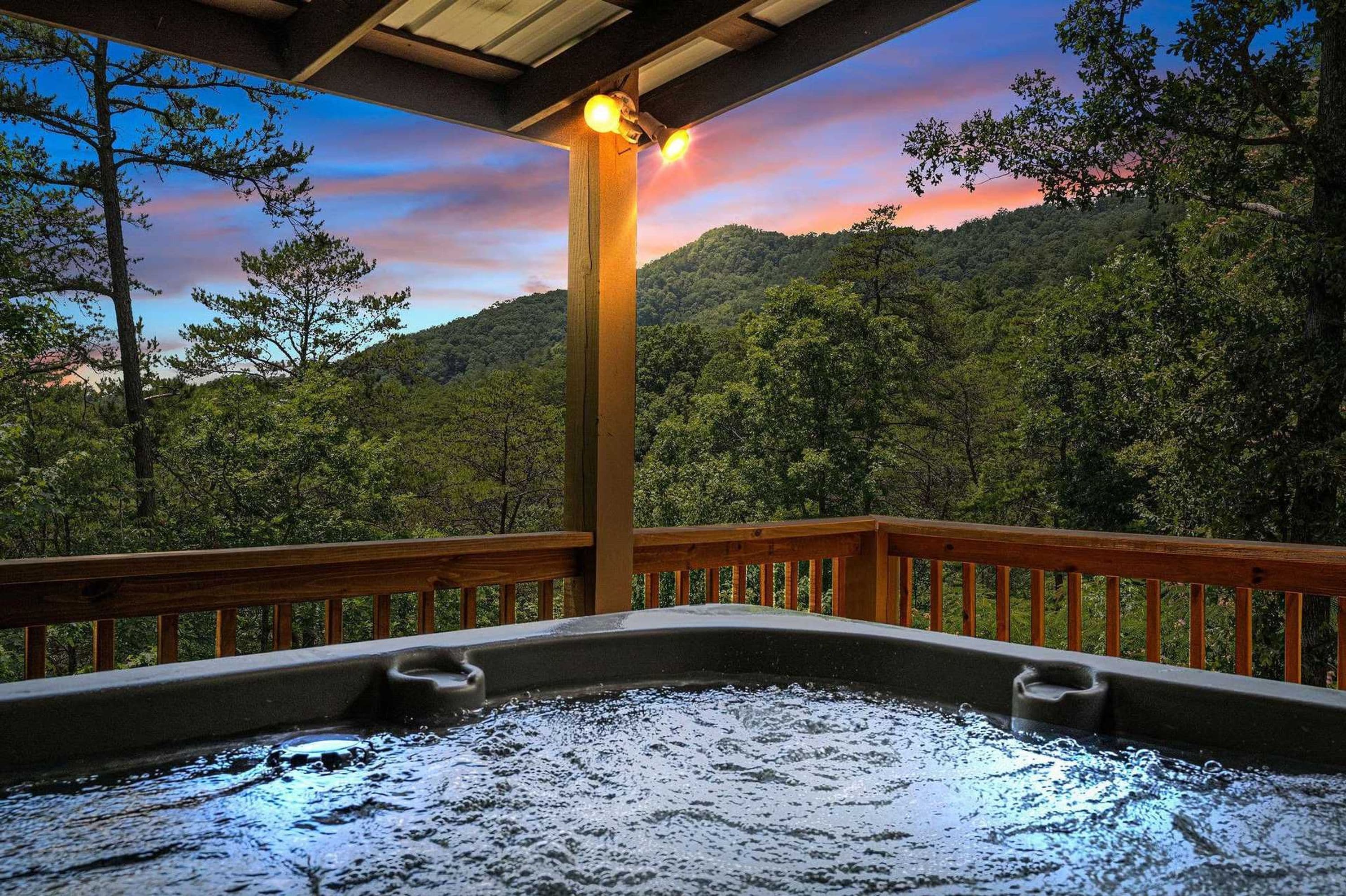 A hot tub under a wooden deck with a view of a forested mountain range.