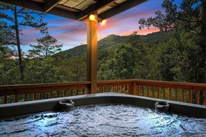 Ein Whirlpool unter einer Holzterrasse mit Blick auf ein bewaldetes Gebirge.