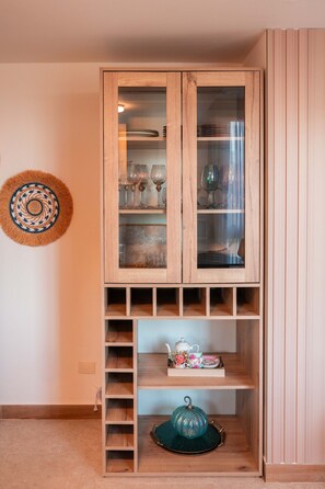 Ein Holzschrank mit Glastüren, der unterschiedliches Glasgeschirr und darunter ein Regal mit Teekanne und Tassen beherbergt.