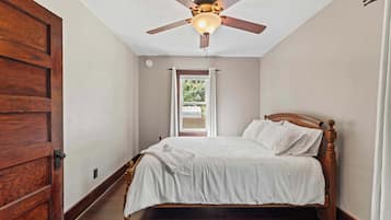 Un dormitorio con cama de madera, ventilador de techo y ventana con cortinas.