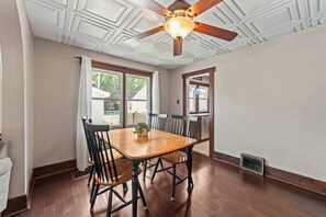 A dining area with a wooden table and chairs, a ceiling fan, and a window with curtains. - Sleeps 7,  2BR-2BA | 5 mins walk to ISU (Ames)