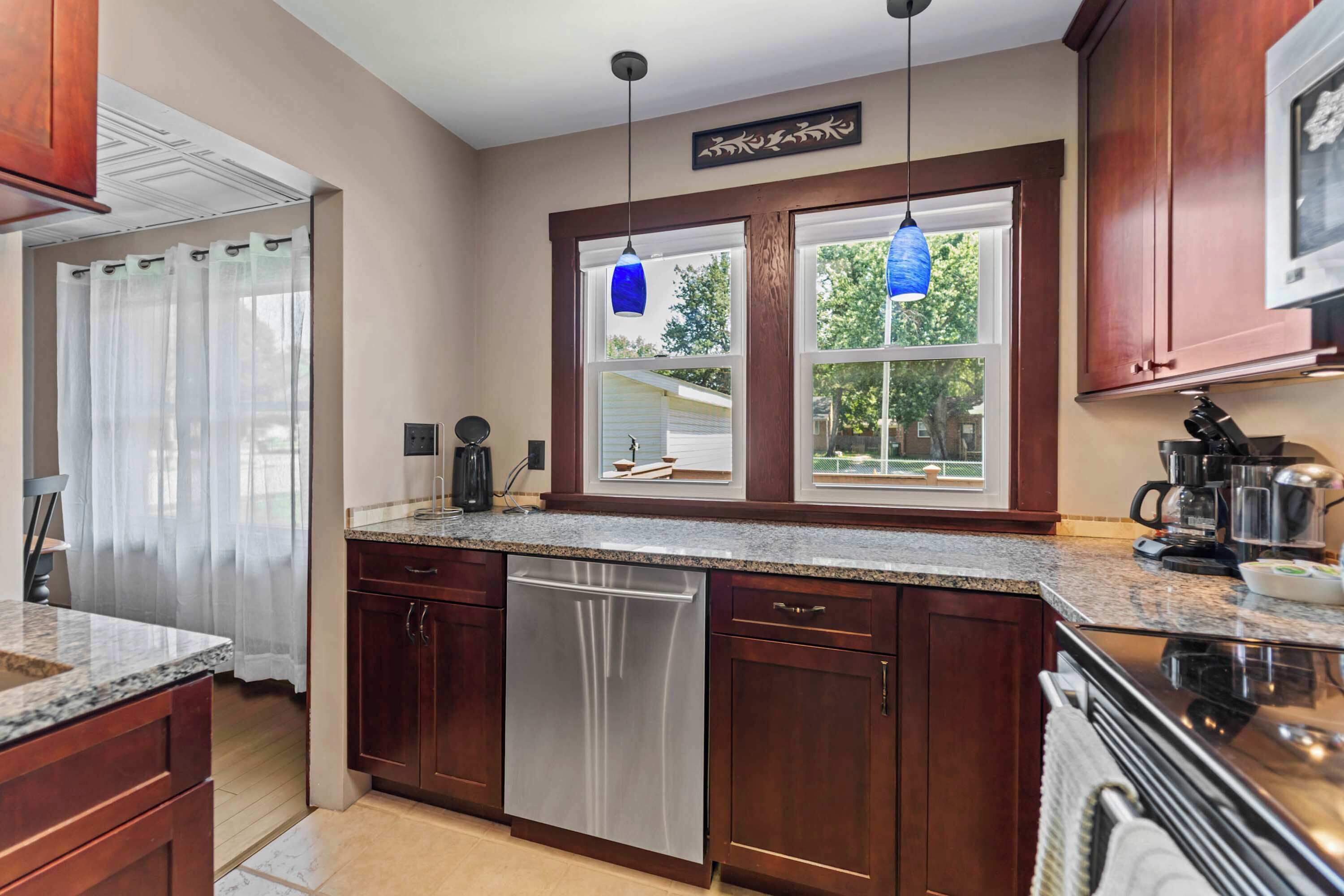A modern kitchen with wooden cabinets, a stainless steel dishwasher, and a window with a view of the outdoors.