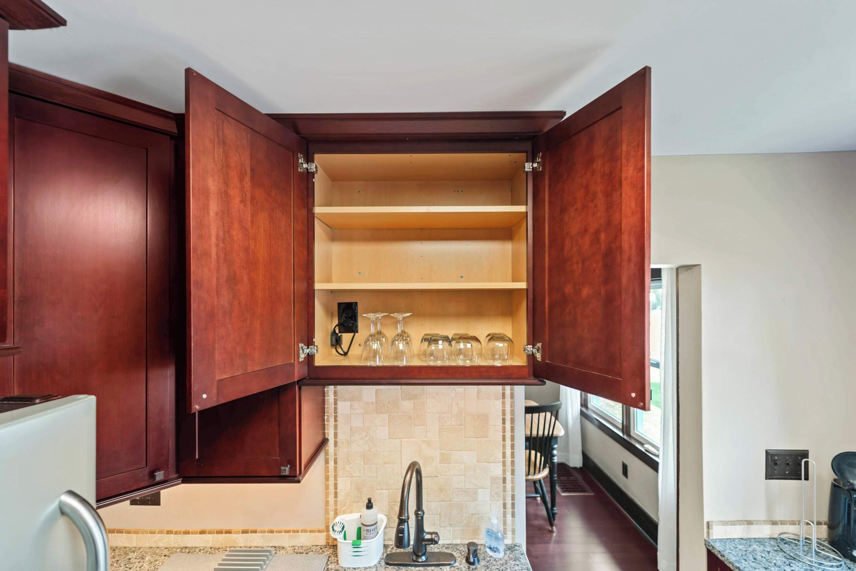 A kitchen with a wooden cabinet open, revealing shelves and a countertop with a faucet and a bottle.