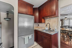 A kitchen with wooden cabinets, a stainless steel refrigerator, a granite countertop, and a tiled backsplash.