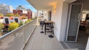 A balcony with a table and chairs, a sliding glass door leading to a dining area, and a view of surrounding buildings. - L Azulejo - Work From Home Ideal - Mobility Lease Rental - 4pax (Toulouse)