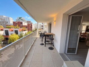 A balcony with a table and chairs, a sliding glass door leading to a dining area, and a view of surrounding buildings. - L Azulejo - Work From Home Ideal - Mobility Lease Rental - 4pax (Toulouse)