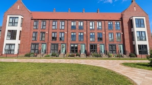 A red-brick building with multiple windows and doors, a green lawn, and a clear blue sky. - Blanket Row (Hull)