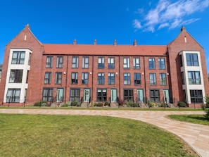 A red-brick building with multiple windows and doors, a green lawn, and a clear blue sky. - Blanket Row (Hull)
