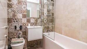 A bathroom with patterned tiles, a toilet, a sink, and a bathtub. - Blanket Row (Hull)