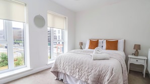 A hotel room with a large bed, two bedside tables, a round mirror, and a view of the city through the window. - Blanket Row (Hull)