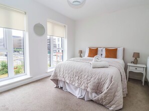 A hotel room with a large bed, two bedside tables, a round mirror, and a view of the city through the window. - Blanket Row (Hull)
