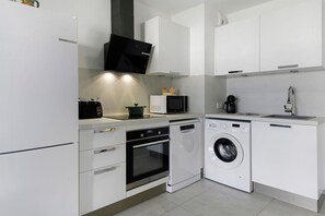 A compact kitchen with white cabinetry, a microwave, a coffee maker, a dishwasher, and a washing machine.
