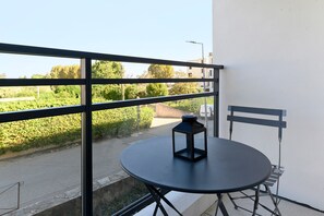 A balcony with a round table and a chair, a small lantern, and a view of a road and greenery.