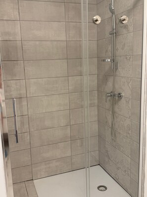 Une douche avec une porte en verre, un pommeau de douche à main et un robinet mural.
