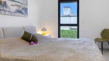 A bedroom with a bed, a chair, a window, and a painting on the wall.