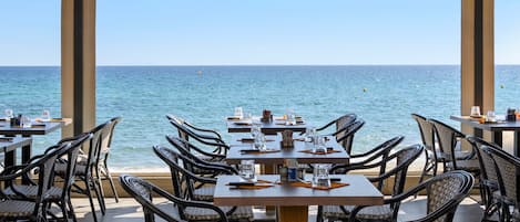 Un área de comedor al aire libre con mesas y sillas frente al mar.
