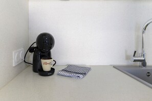Une machine à café avec une tasse posée sur un plan de travail, à côté d’un évier.