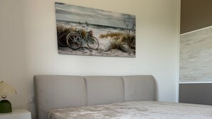 A bedroom with a bed, a nightstand, a lamp, and a painting of a beach scene.
