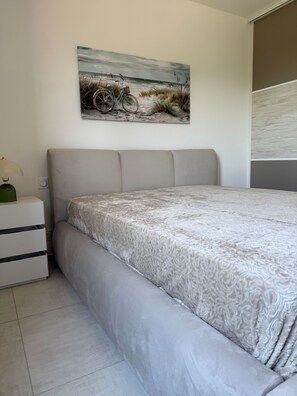 Une chambre à coucher avec un lit, une table de chevet, une lampe et un tableau représentant une scène de plage.