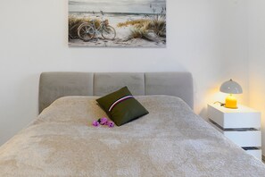 A bedroom with a bed, a pillow, a bedside table with a lamp, and a wall-mounted picture.