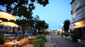 An outdoor seating area with tables and chairs, umbrellas, and potted plants along a street.
