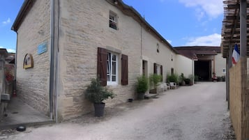 A stone building with a gravel driveway, wooden shutters, and potted plants.