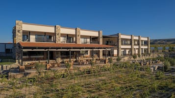 Ein mehrstöckiges Gebäude mit Außenbestuhlung und einem Weinberg im Vordergrund.