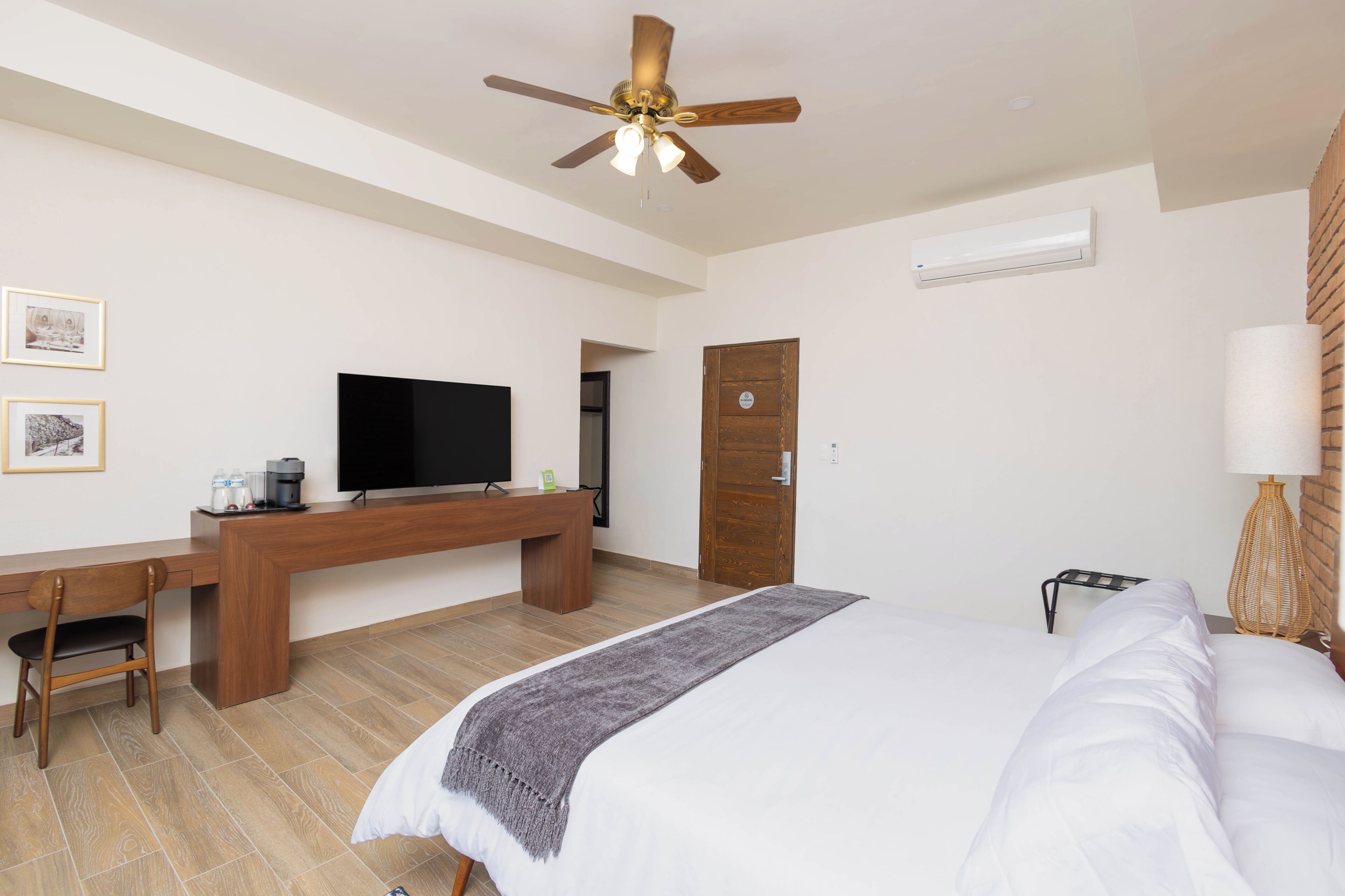 Ein Hotelzimmer mit Bett, Schreibtisch, Stuhl, Fernseher, Deckenventilator und einer Tür.