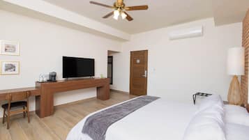 Ein Hotelzimmer mit Bett, Schreibtisch, Stuhl, Fernseher, Deckenventilator und einer Tür.