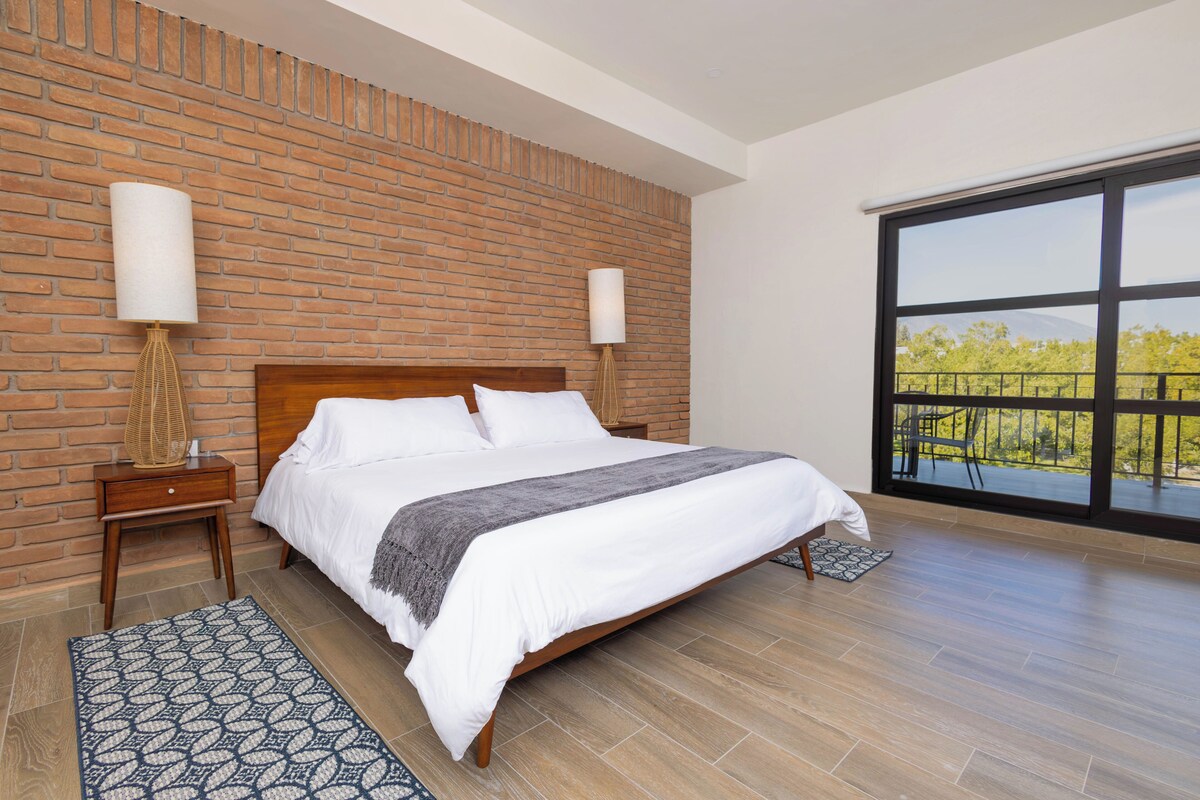 Una camera da letto moderna con parete in mattoni, un letto grande, due lampade da comodino e vista attraverso un'ampia finestra.
