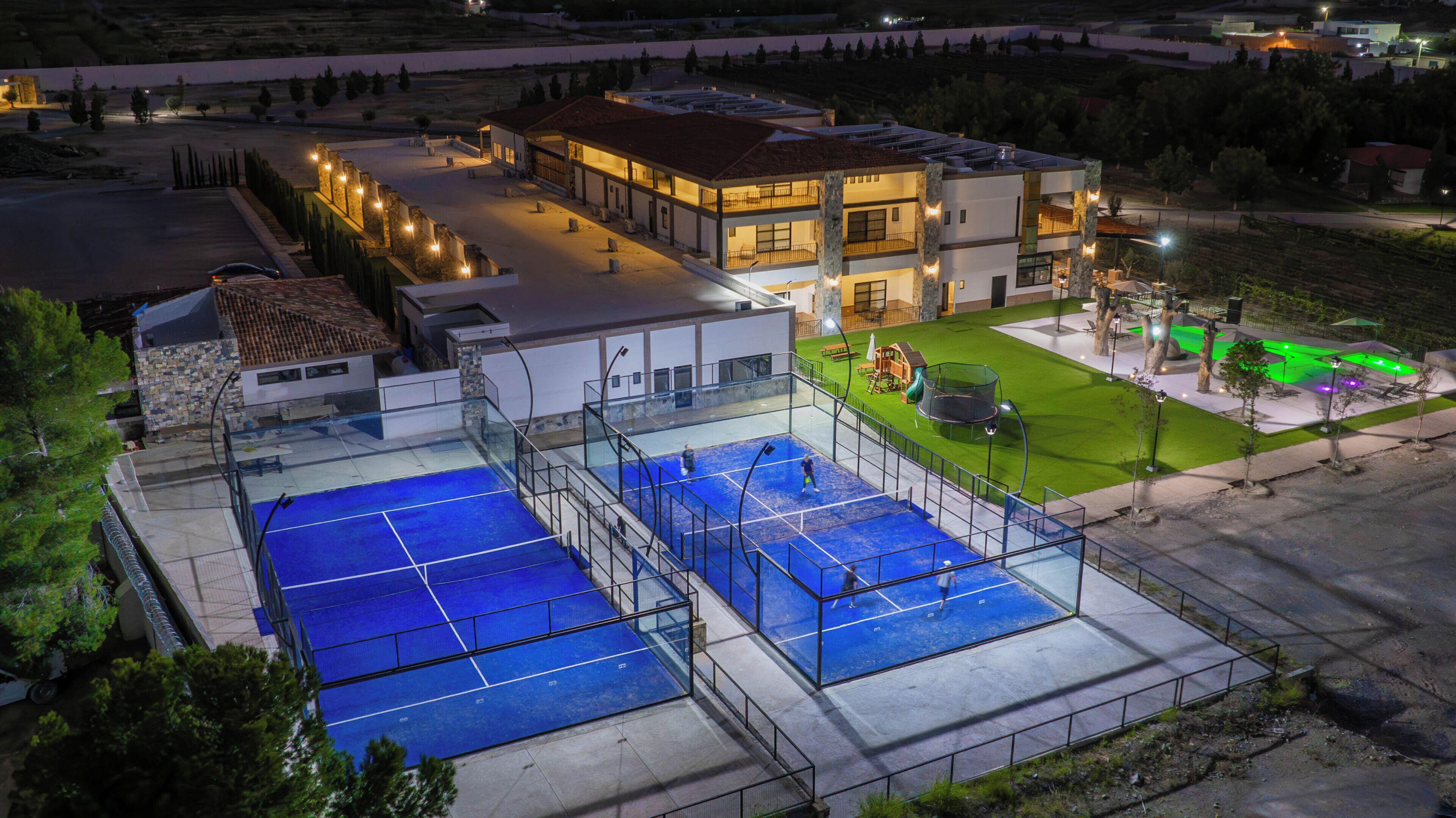 Ein Tennisplatz mit Netz, umzäunt und neben einem Gebäude mit mehreren Fenstern und Balkonen.
