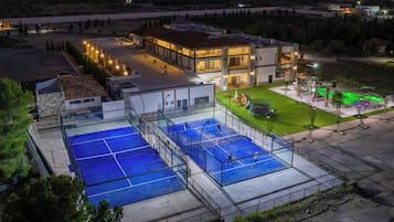 Ein Tennisplatz mit Netz, umzäunt und neben einem Gebäude mit mehreren Fenstern und Balkonen.