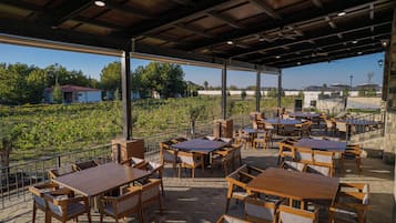 Eine Außenpatio mit mehreren Holztischen und -stühlen, einem Metallgeländer und Blick auf einen Weinberg.