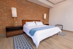 A hotel room with a brick wall, a wooden bed, two bedside tables, and a patterned rug.