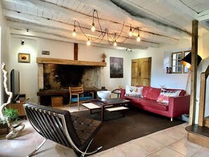 A living room with a fireplace, a red sofa, a black chair, and a wooden table. - Ground-floor room with a separate entrance (Veyrines-de-Domme)