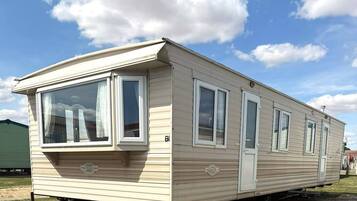 A mobile home with a front porch, large windows, and a door.