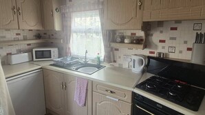 A compact kitchen with a microwave, sink, kettle, and stove.
