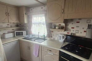 A compact kitchen with a microwave, sink, kettle, and stove.