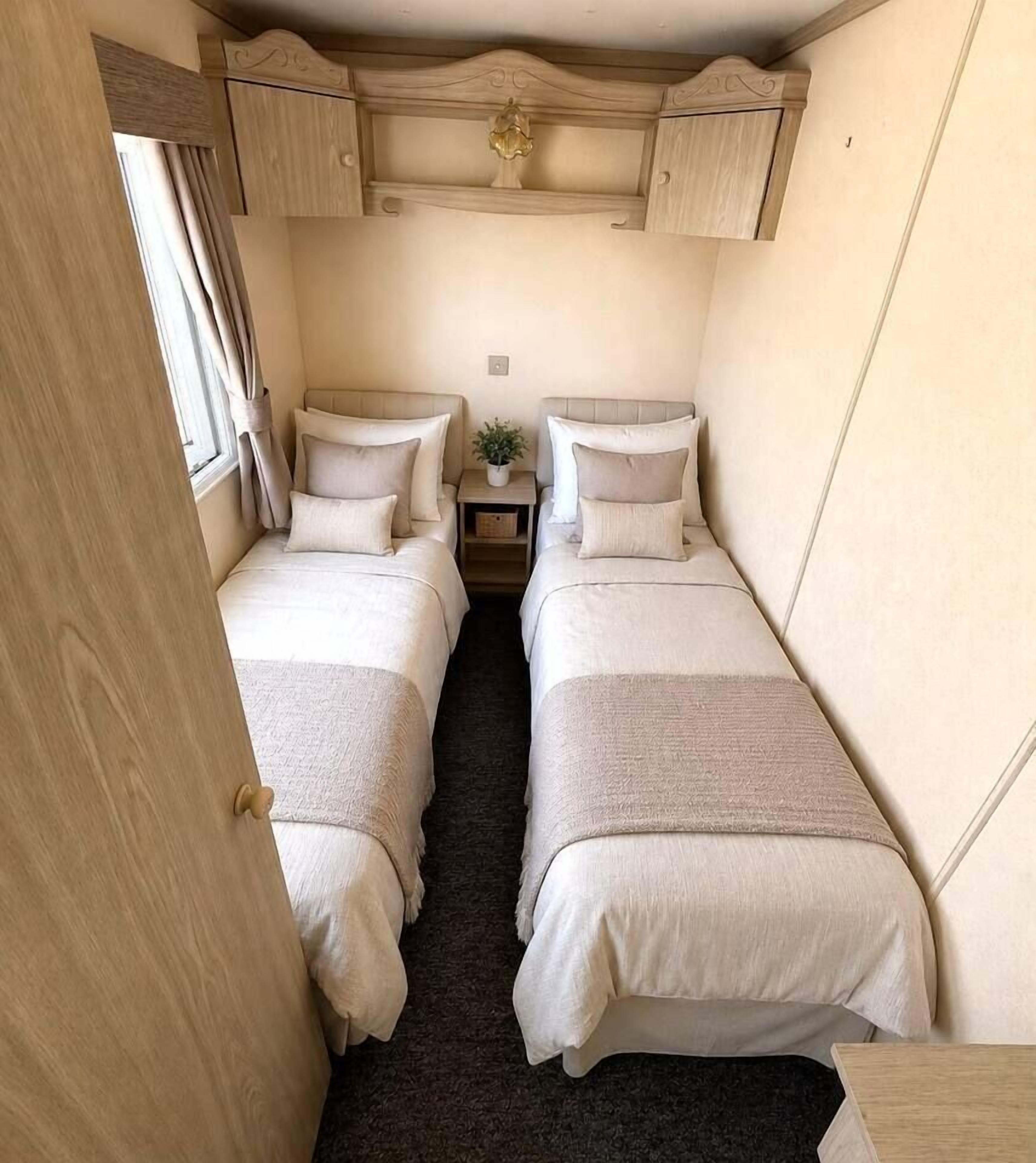Ein kleines Schlafzimmer mit zwei Betten, einem Nachttisch und einem Fenster mit Vorhängen.