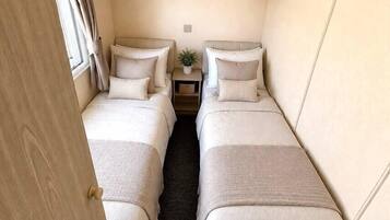 Ein kleines Schlafzimmer mit zwei Betten, einem Nachttisch und einem Fenster mit Vorhängen.